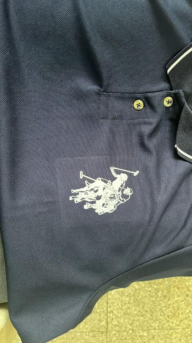 Dark blue polo shirt with a logo on the chest against a yellow floor background